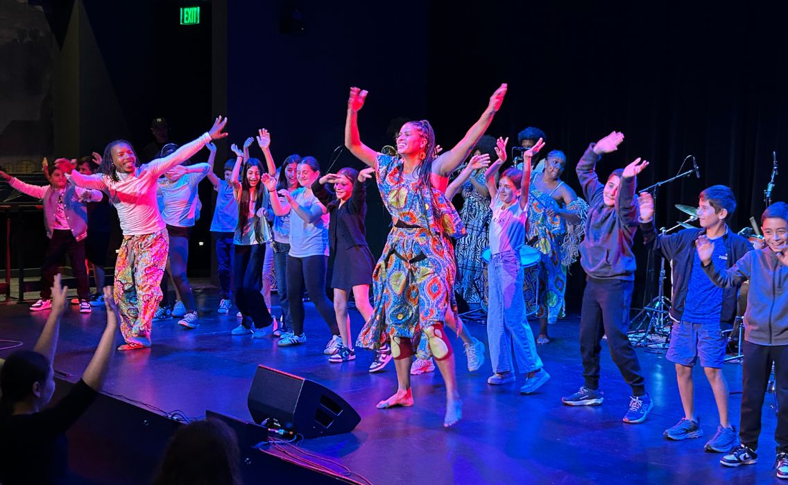 Performers and students raise their arms in the air and dance with multicolor lights