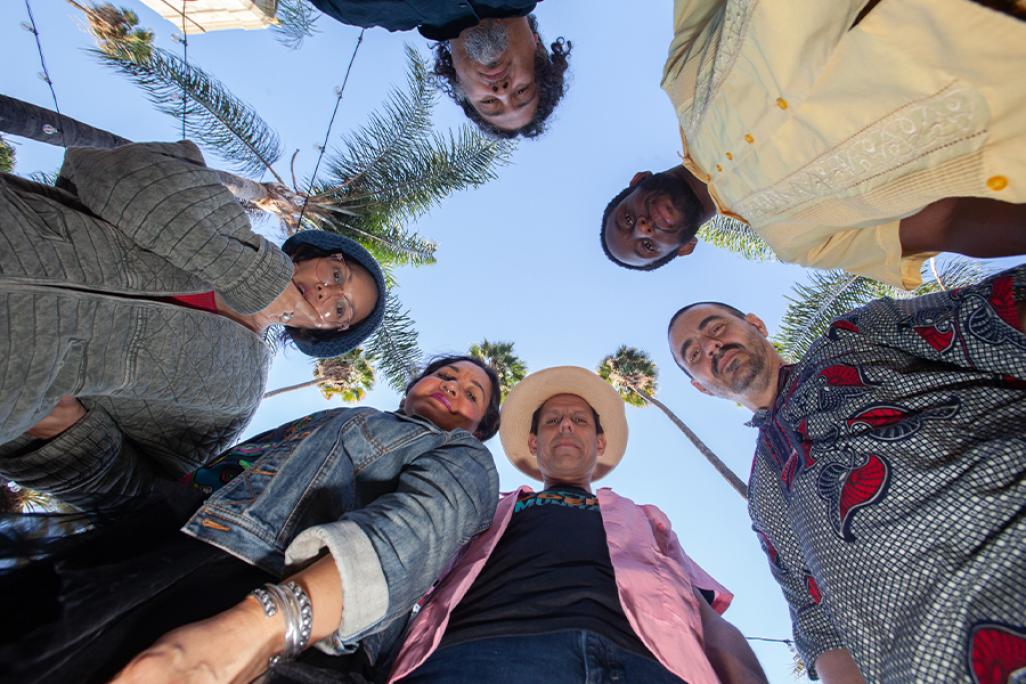 Image of members of Quetzal standing in a circle, looking downwards at the camera