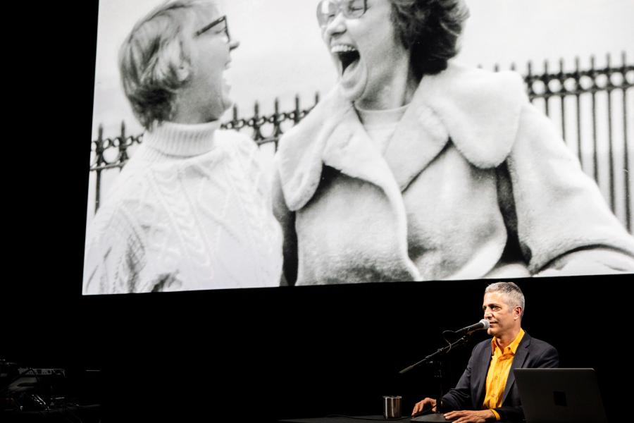 Sam Green on stage with a black and white photo displayed behind him 900x600