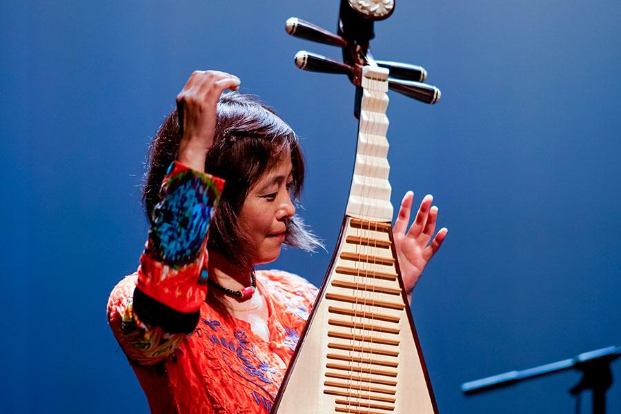 Wu Man performs on stage in front of a blue background