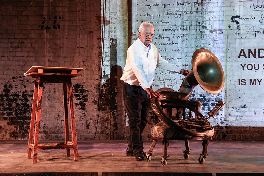 Image of a performer on stage wheels out a large horn seated on top of a chair