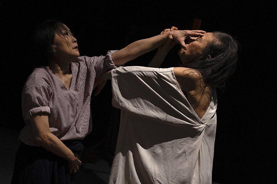 Eiko Otake and Wen Hui perform together on stage in front of a black backdrop