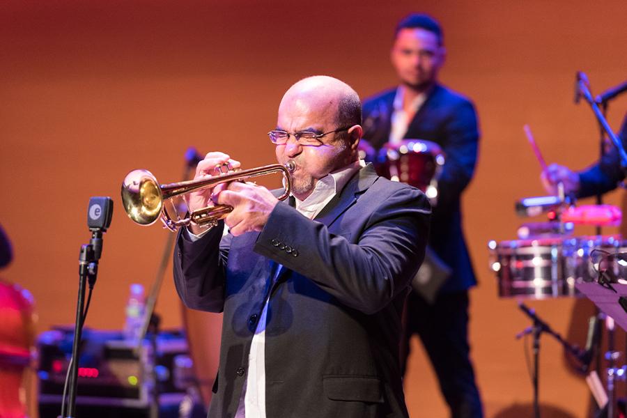 Member of Orquesta Akokán plays the trumpet on a stage with an orange backdrop