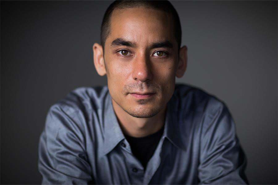 Headshot of Andy Akiho wearing a blue button down shirt with a gray background