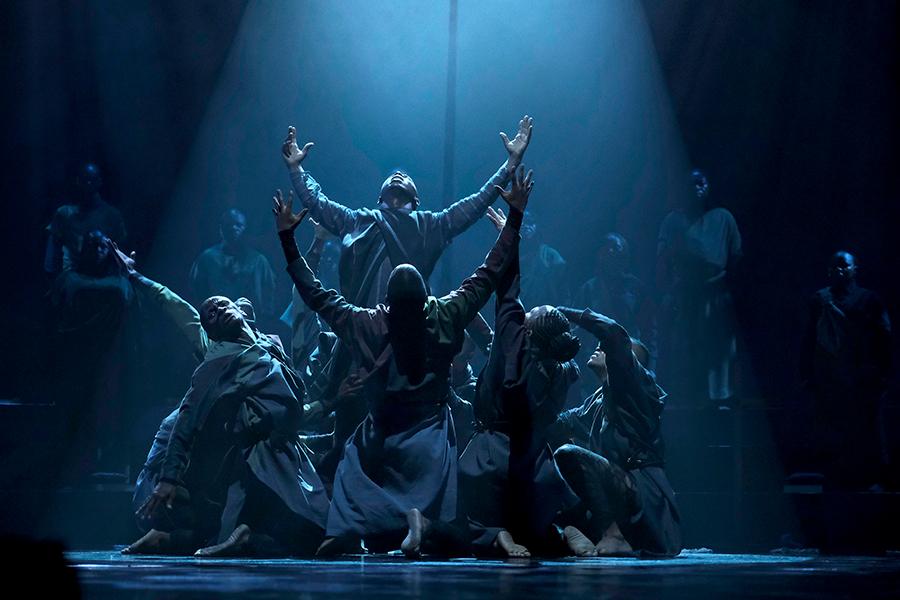 Dancers perform under a blue light in a pyramid formation