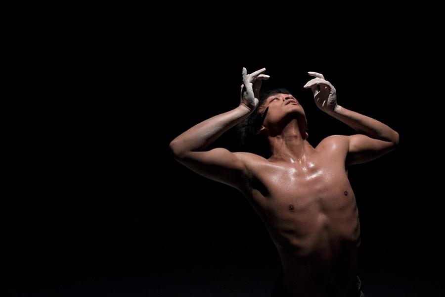 Rianto performs on stage in front a black backdrop with their hands lifted above their shoulders