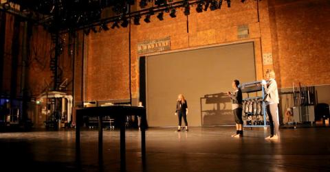 Image of the inside of Freud Playhouse, featuring a piano and three artists standing and rehearsing